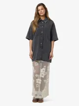 Vestido camisero corto de denim negro con lavado ácido, manga corta, cierre frontal con botones, dos bolsillos con solapa en el pecho y corte holgado.