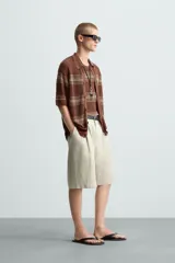 Camisa de punto de manga corta, color marrón rojizo con rayas horizontales en tono beige/verde oliva. Presenta cuello solapa y cierre frontal de botones.