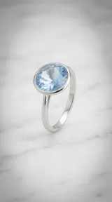 Anillo de plata con engaste circular y cristal facetado de color celeste.