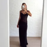 Vestido largo negro, ajustado al cuerpo, con escote en V y tirantes finos. La parte superior del corpiño es de tejido con brillo o lentejuelas, y el resto del vestido es de tela semitransparente o gasa, con un forro opaco que cubre desde la cadera hacia abajo.