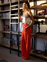 Pantalón naranja de crepe elastizado, corte recto, con bolsillos delanteros y apliques de botones metálicos.