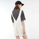 Enterito corto oversize de color blanco, con diseño de peto, tirantes ajustables con hebilla metálica y bolsillos frontales.