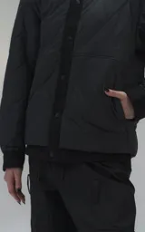 Campera tipo sobrecamisa de diseño oversize, confeccionada en microfibra opaca con patrón matelaseado geométrico. Presenta cuello, puños, cartera central y ruedo en gabardina de algodón, con cierre frontal mediante broches a presión. El diseño del ruedo simula una prenda superpuesta.