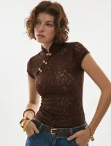 Top de encaje floral color chocolate, con cuello estilo mandarín y cierre frontal con broches ornamentales dorados. Presenta un calce ajustado al cuerpo y mangas cortas.