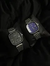 Reloj Casio Quartz con caja cuadrada plateada, esfera azul intenso, manecillas y marcadores de hora dorados, y correa de acero inoxidable plateada. Incluye función de fecha.