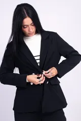 Blazer negro levemente largo, con solapas de muesca, doble botonadura con botones metálicos dorados, hombreras y bolsillos delanteros ribeteados con solapa.