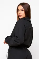 Buzo cropped negro de estilo urbano, con cuello alto ajustable mediante cordón, mangas largas con puños elásticos y cintura con ajuste regulable.