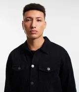 Campera de sarga negra, modelo trucker, con cuello camisero, recortes, dos bolsillos delanteros con solapa y abotonado total.