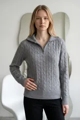 Sweater de punto gris con diseño de ochos verticales, cuello alto con cierre frontal y mangas largas con puños acanalados.