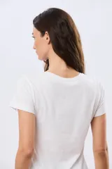 Remera blanca de manga corta y cuello redondo, con estampa frontal de flores en tonos rosados dentro de un frasco de vidrio y detalles de letras bordadas.
