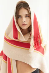 Ruana artesanal de tejido de punto, color beige con franjas horizontales gruesas rojas y finas amarillas. Posee flecos en el borde inferior.