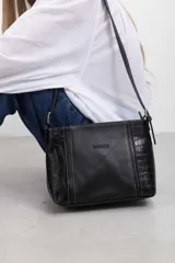 Cartera bandolera de cuero color negro, de diseño estructurado con panel central liso y laterales con textura efecto croco. Cuenta con correas ajustables y costuras a contratono.
