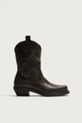 Bota estilo cowboy de caña media, confeccionada en cuero con acabado desgastado. Presenta horma cuadrada, tiradores laterales y suela con tacón bloque.