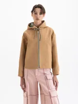 Chaqueta color camel con capucha, cierre frontal y bolsillos laterales. Presenta un diseño de corte recto y forro interior a cuadros, con detalle de bordado en el pecho.