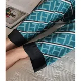 Conjunto de pijama de dos piezas compuesto por una camisa de manga larga con cuello mao y cierre frontal de botones, y un pantalón largo. Presenta un diseño estampado de corazones sobre fondo negro con detalles en color blanco.