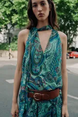 Top sin mangas de cuello alto con lazo ajustable, escote en V y diseño cruzado en el delantero. Presenta un estampado paisley en tonos verdes, azules y rosados, con bajo elástico y forro interior.