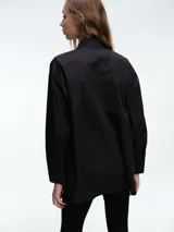 Camisa de corte holgado y líneas clásicas, confeccionada en algodón. Presenta cuello camisero, cierre frontal mediante botones y detalle de botones en los laterales para ajustar la silueta.