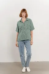 Camisa verde menta de tela arrugada, con cuello clásico, botones frontales, mangas cortas y dos bolsillos delanteros con pespuntes. La base es levemente elastizada y se anuda en el frente.