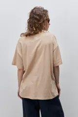 Remera color tostado de corte holgado, con cuello redondo y mangas cortas. Presenta un estampado gráfico frontal de estilo veraniego con ilustraciones de una langosta, conchas, limón, una copa y la inscripción 'Summer Club'.