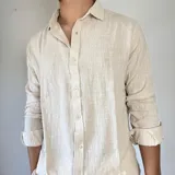 Camisa de lino con corte oversize, cuello clásico y cierre frontal con botones. Presenta mangas largas con puños arremangados y una textura rústica característica del tejido.