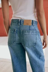 Jeans de tiro medio con pernera holgada tipo barrel que se estrecha hacia el tobillo, acabado con bajo sin costura, bolsillos delanteros y bolsillos de plastrón en la espalda. Cierre frontal con cremallera y botón.