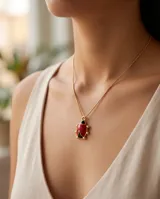 Collar de bronce con cadena fina dorada y un dije colgante en forma de mariquita con detalles esmaltados en rojo y negro.