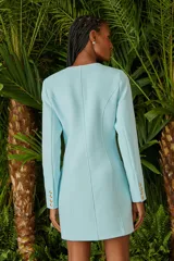 Vestido corto celeste con escote en V cruzado, mangas largas y botones dorados.