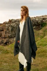 Ruana de tejido grueso color gris oscuro, con flecos en el borde inferior y etiqueta de cuero con logo de la marca.