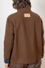 Campera de paño de lana color marrón con diseño oversize. Presenta cuello alto, cierre frontal con botones y detalles en pana azul marino en los puños y en las tapas de los bolsillos frontales.