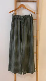 Pantalón de corte ancho y relajado, confeccionado en lino con diseño de rayas verticales. Presenta cintura elástica con cordón de ajuste y bolsillos laterales.