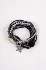 Set de pulseras elásticas de cuentas en tonos negros, plateados y grises. Incluye un dije de estrella de mar metálica, un dije de caracol natural y un pompón negro decorativo.