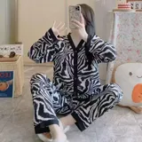 Conjunto de pijama de dos piezas compuesto por una camisa de manga larga con cuello mao y cierre frontal de botones, y un pantalón largo. Presenta un diseño estampado de corazones sobre fondo negro con detalles en color blanco.
