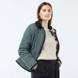 Chaqueta corta con estampado floral en tonos rosa y celeste sobre fondo negro. Tiene cuello mao y cierre frontal con botones a presión.