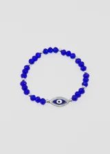 Pulsera elástica con mostacillas facetadas color azul y mostacillas plateadas. Dije central con forma de ojo turco con borde plateado y pupila blanca sobre fondo azul.