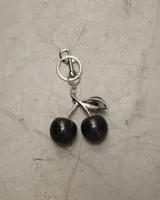 Llavero con dije de dos cerezas negras brillantes y hoja plateada.