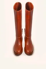 Bota de caña alta confeccionada en cuero vacuno suave, con diseño minimalista y suela de goma robusta. Presenta costuras visibles en la zona del empeine y un taco bajo cuadrado.