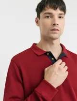 Remera de manga larga con cuello polo, confeccionada en tejido de punto canalé francés. Presenta abotonadura frontal con botones de madera y detalles a contratono en la cartera y el interior del cuello.