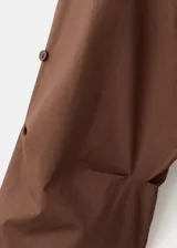 Camisa de algodón color marrón, de diseño recto, con cuello camisero, manga larga con puños abotonados y cierre delantero con botones.