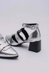 Sandalias plateadas con punta cerrada, tiras entrecruzadas y pulsera al tobillo con hebilla. Taco cuadrado negro.