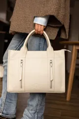 Cartera de cuero color tostado, estructurada, con doble asa de mano, correa desmontable y dos bolsillos frontales verticales con cierre. Presenta detalles de costuras pespunteadas y el logo de la marca grabado en la parte inferior.