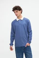 Remera polo de manga larga azul con cuello camisero blanco y cierre frontal de botones ocultos. Presenta un pequeño bordado con el texto "uniform" en el pecho y calce relajado.