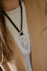 Collar largo con cordón negro y dije colgante de metal plateado con diseño orgánico y texturizado.