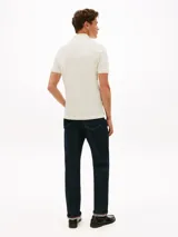 Chomba de piqué de algodón mercerizado color blanco hueso, con cuello de chomba y cartera con cremallera. Presenta un logo Tommy Hilfiger bordado en el pecho.