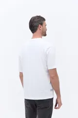 Remera de manga corta color beige, con cuello redondo y estampa gráfica central con motivos botánicos y texto.