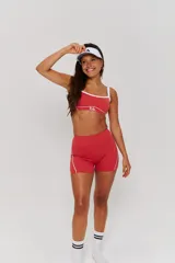 Conjunto deportivo compuesto por un top y un short de tiro alto en color bordó con detalles de líneas blancas. El top presenta breteles anchos y el logo de la marca en el frente, mientras que el short tiene un diseño ajustado con costuras laterales visibles.