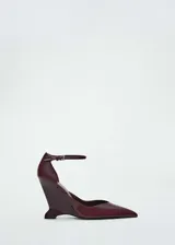 Zapato de tacón color borgoña charolado, con punta fina, tacón de cuña y pulsera al tobillo con hebilla.