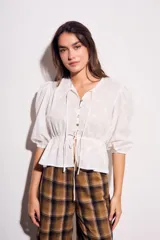 Blusa negra de algodón con diseño de broderie, mangas tres cuartos abullonadas, cierre frontal con botones y detalle de cordón ajustable en la cintura.