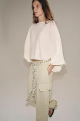 Cuerpo de punto color crudo, con cuello barco y mangas largas abullonadas con sisa ancha y puños ajustados.