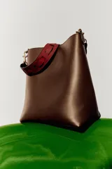 Bolso de hombro tipo saca en color marrón, con diseño minimalista y cierre de clip metálico. Incluye una correa de hombro con detalles troquelados en contraste y herrajes dorados.