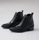 Bota corta de cuero vacuno color negro, con diseño combinado de cuero liso y cuero con textura de reptil en el empeine. Presenta punta fina, taco cuadrado de 6 cm y doble cierre lateral.